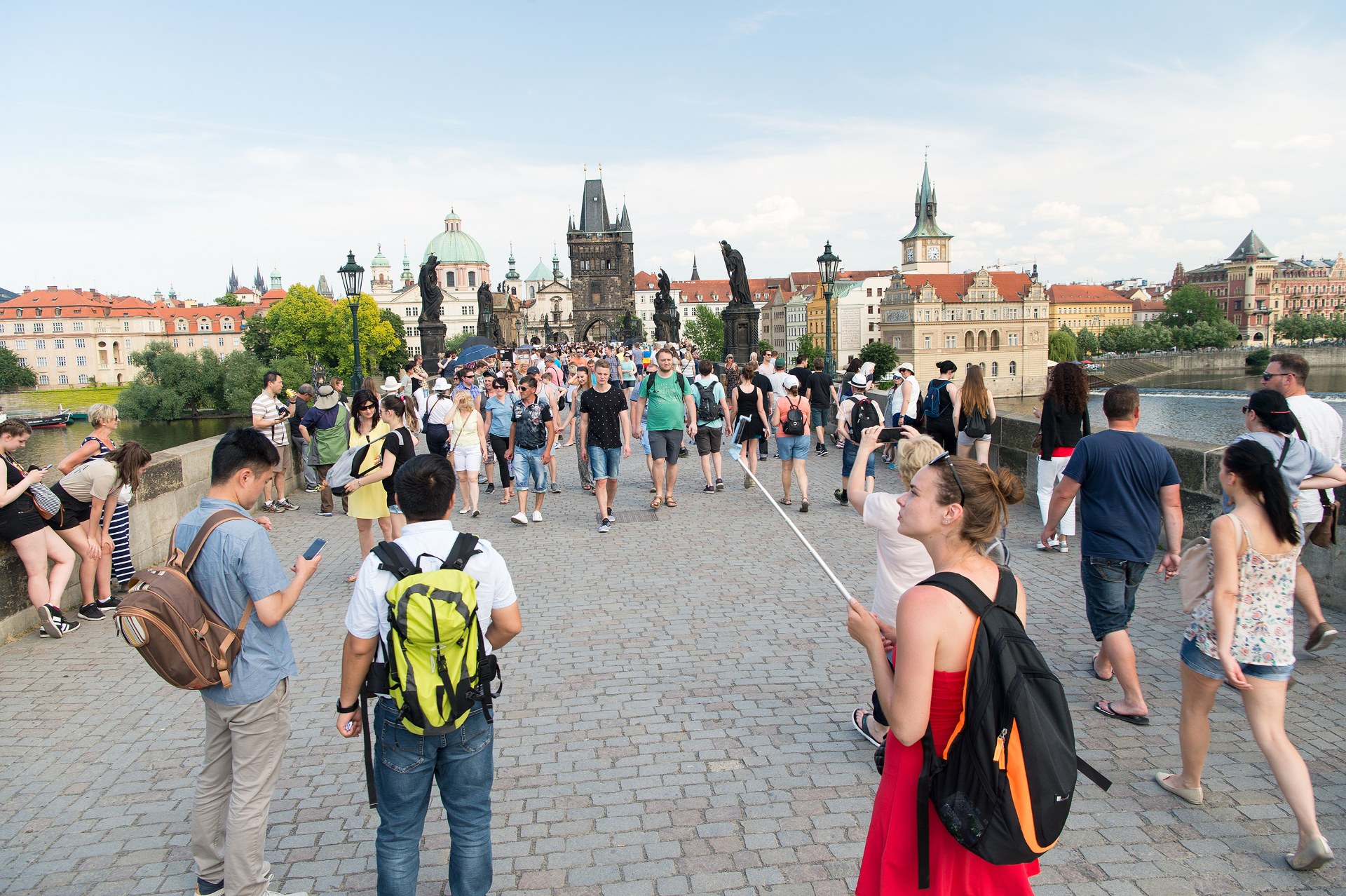 Jovens de mochila às costas a atravessar a Ponte Carlos, em Praga, com a torre da ponte da Cidade Velha ao fundo
